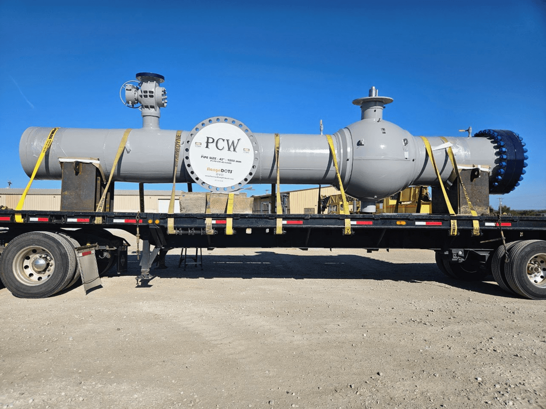 Large PCW industrial equipment strapped on a flatbed truck, ready for transport under a clear blue sky