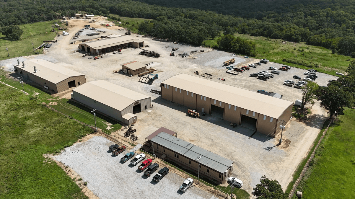 Aerial view of an industrial facility with multiple buildings, parking areas, and surrounding greenery