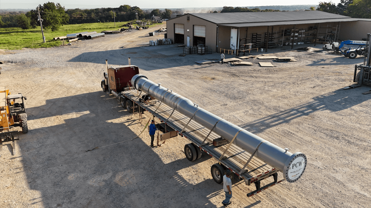 Aerial view of large industrial equipment secured on a flatbed truck at an industrial site, with workers preparing for transport