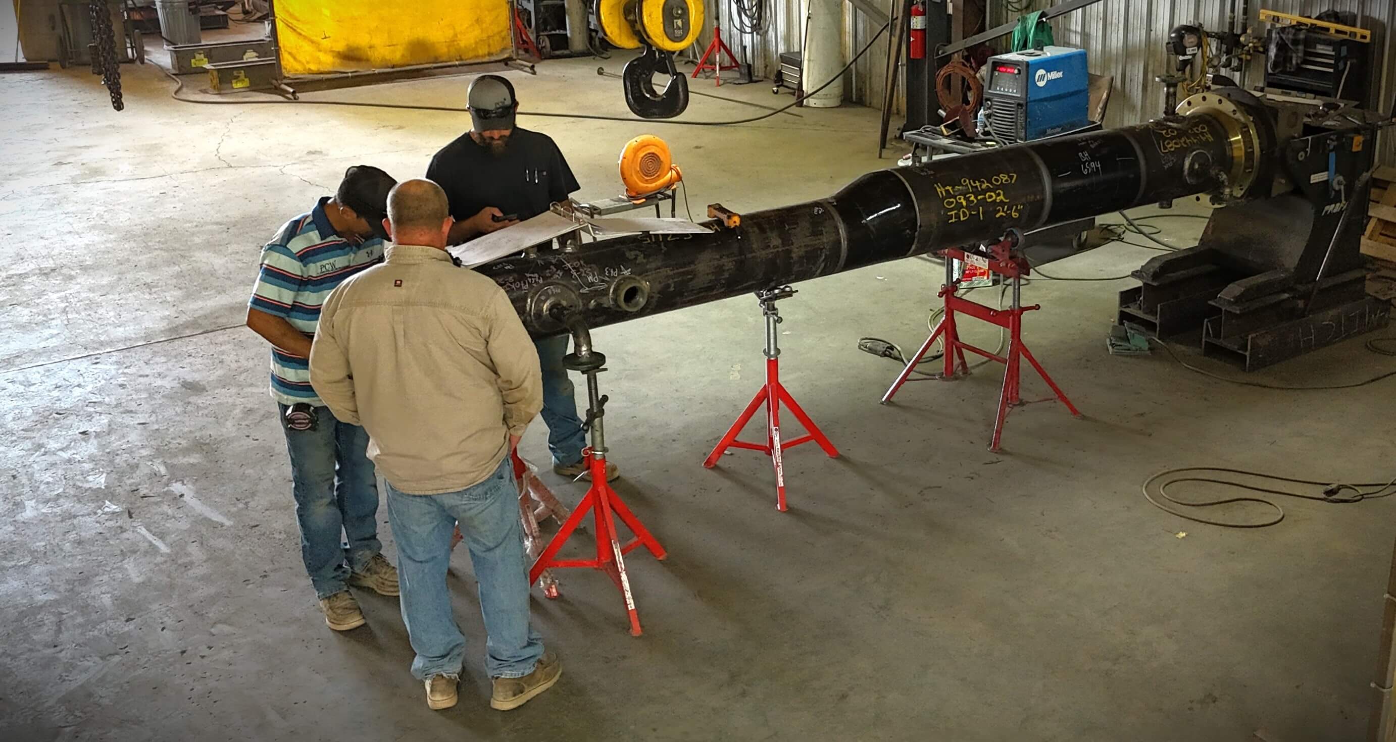 Three technicians inspecting a large industrial component in a workshop, discussing measurements and adjustments