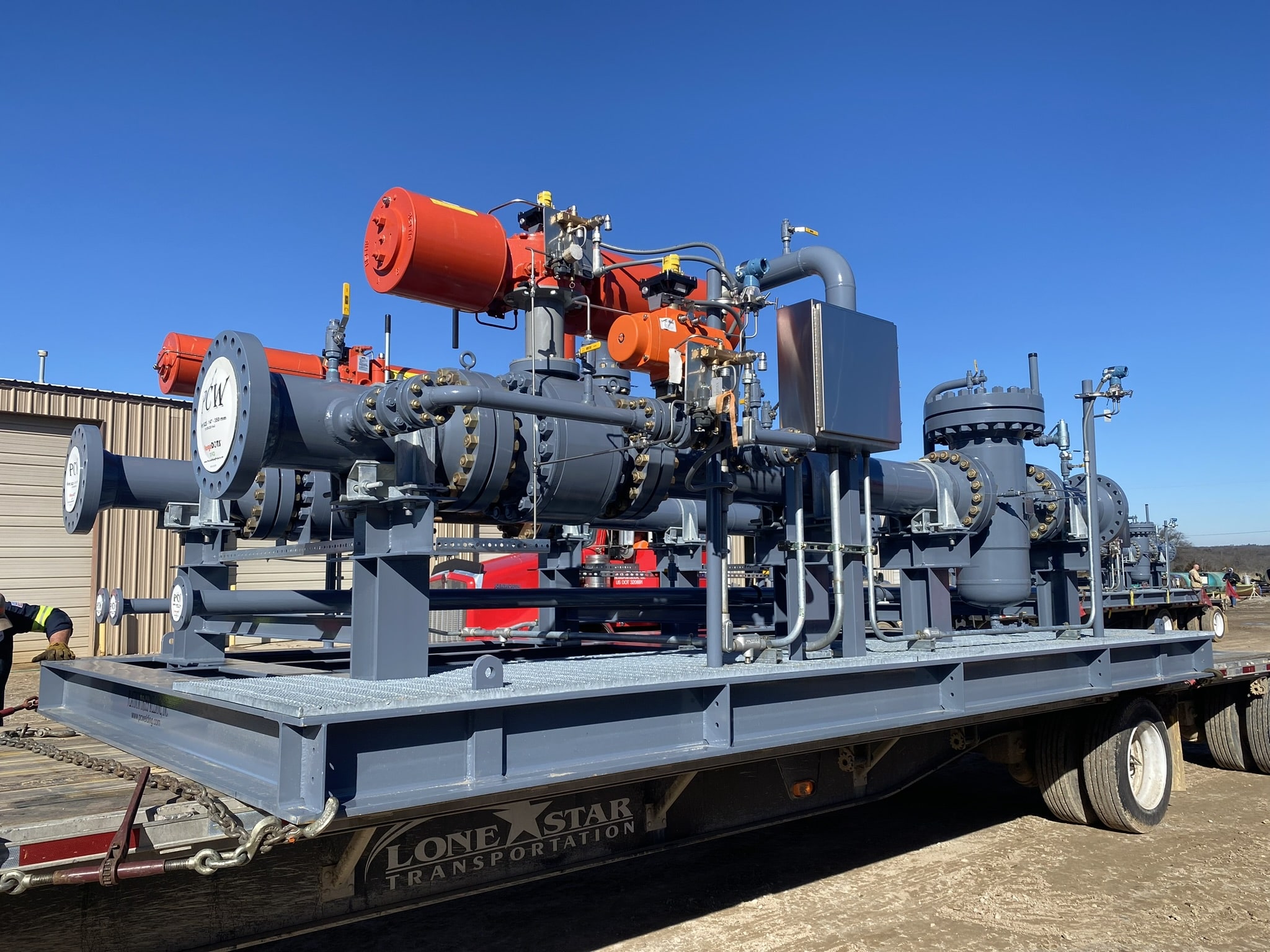 Industrial equipment skid with various valves and control systems mounted on a trailer, under a clear sky