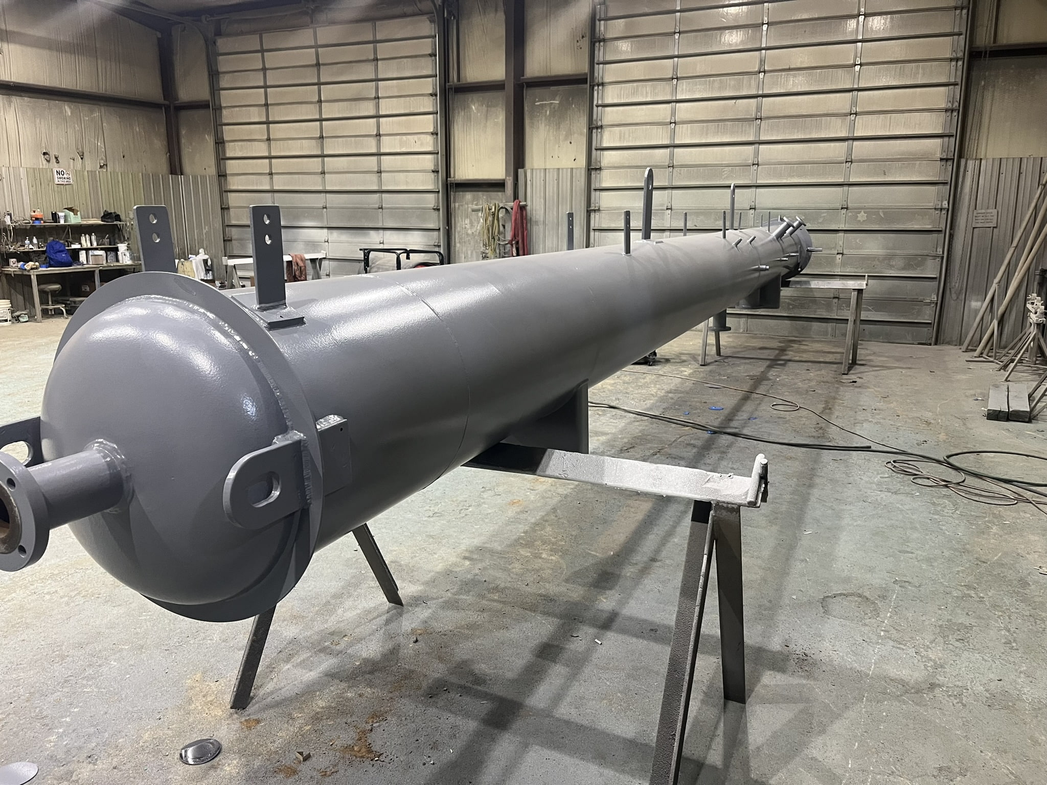 Long gray industrial pipe structure in a workshop setting with tools and equipment in the background