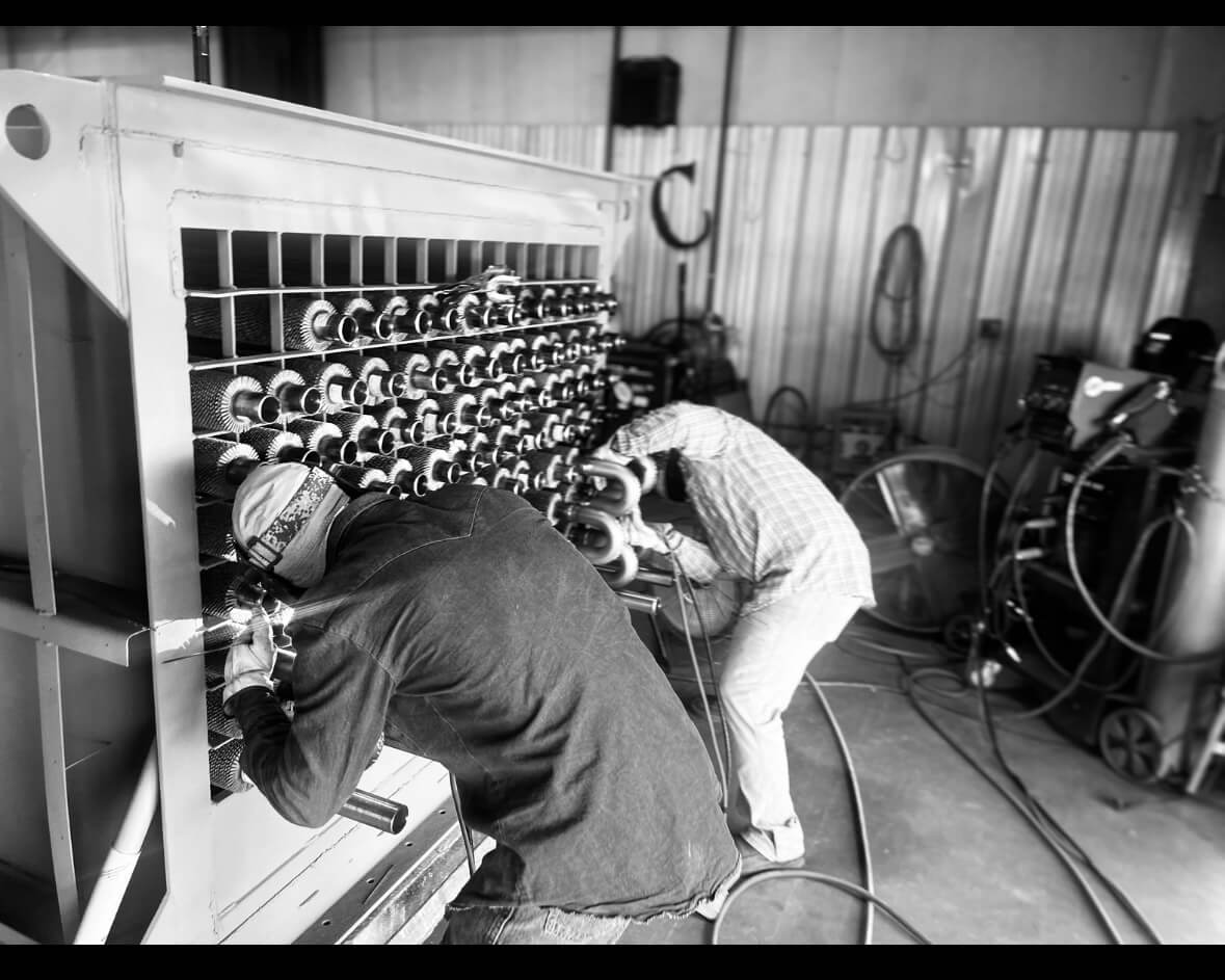 Two welders working on an industrial heat exchanger, performing welding on metal tubes in a workshop