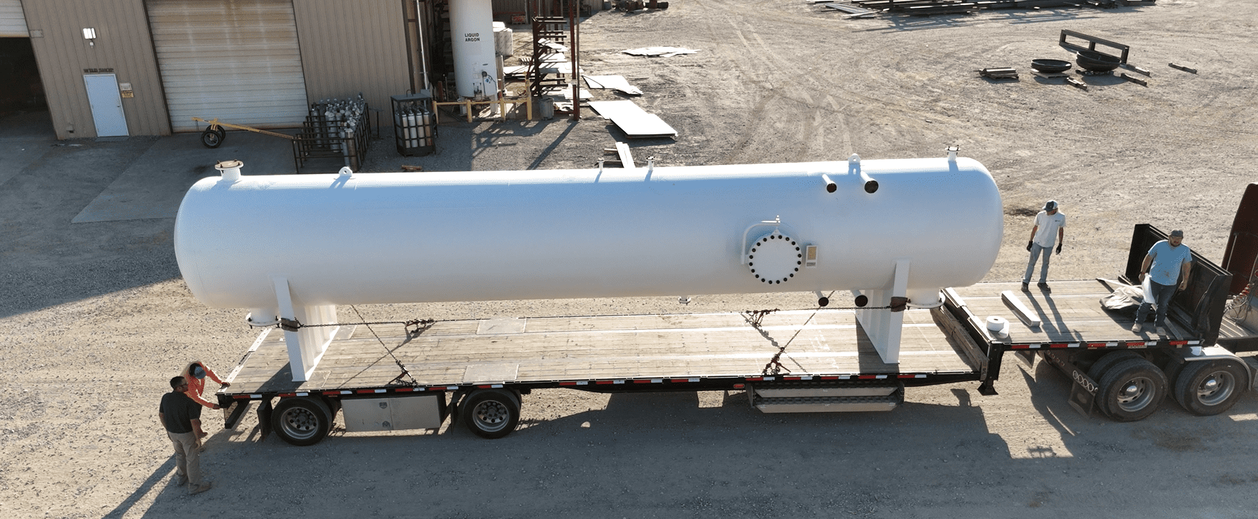 Large white industrial tank secured on a truck for transport with workers standing nearby