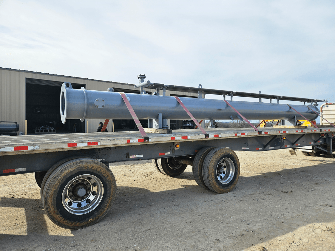 Long gray industrial pipe secured on a flatbed truck for transport outside a workshop