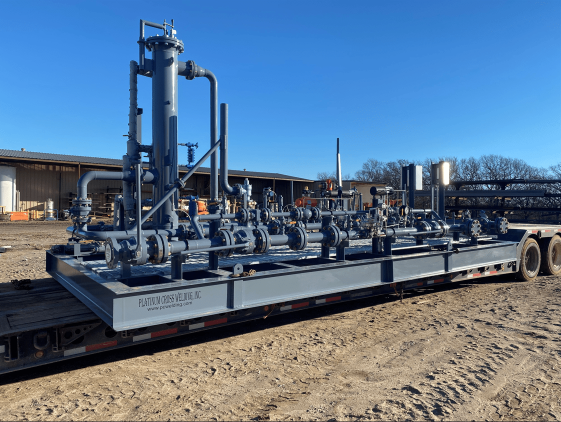 Industrial skid-mounted equipment on a trailer, featuring pipes, valves, and control systems under a clear blue sky